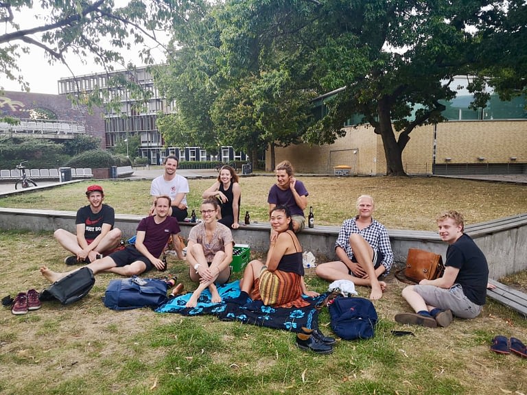 Mitglieder der Lokalgruppe Hamburg sitzen in sommerlicher Kleidung im Gras vor einem Universitätsgebäude.