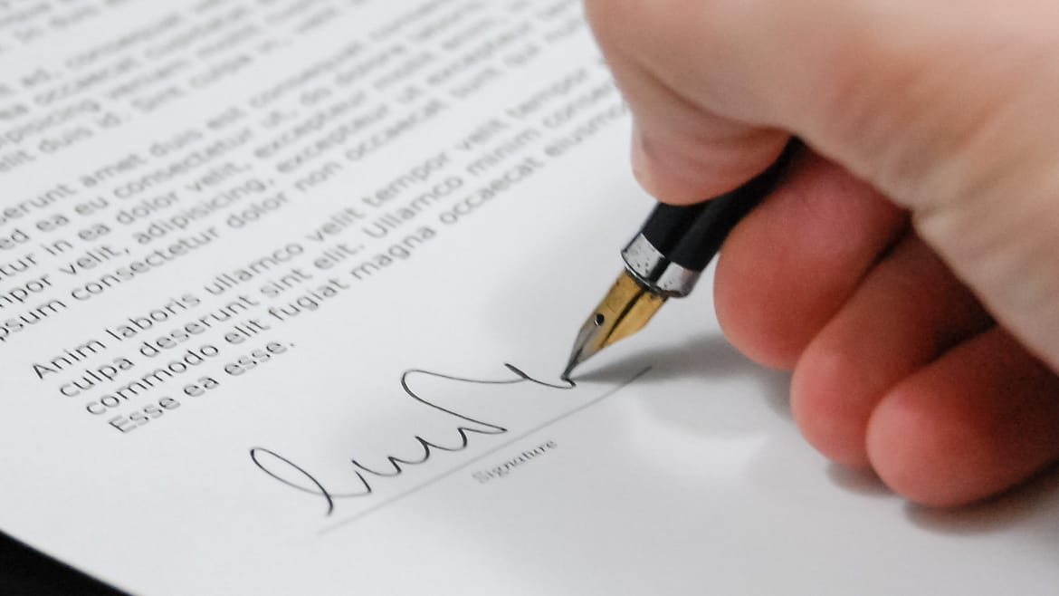 Hand, die mit einem Füller ein Dokument unterzeichnet.